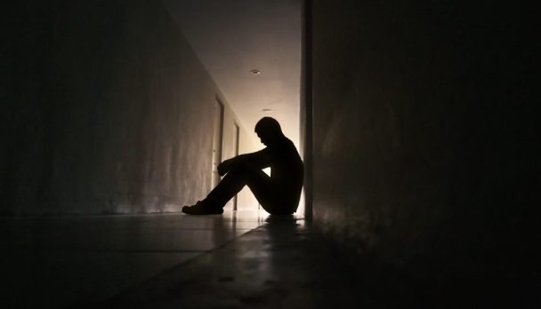 Silhouette,Of,Depressed,Man,Sitting,On,Walkway,Of,Residence,Building.